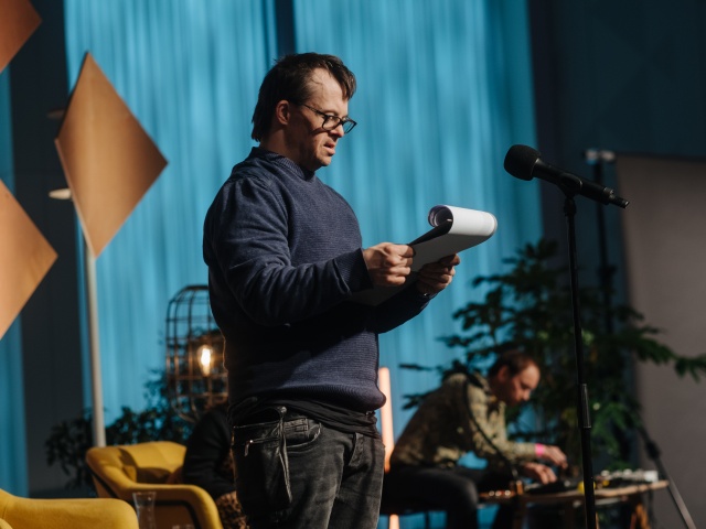 Ein Mann mit Down-Syndrom steht auf einer Bühne und liest einen Text von einer Klemmmape ab.