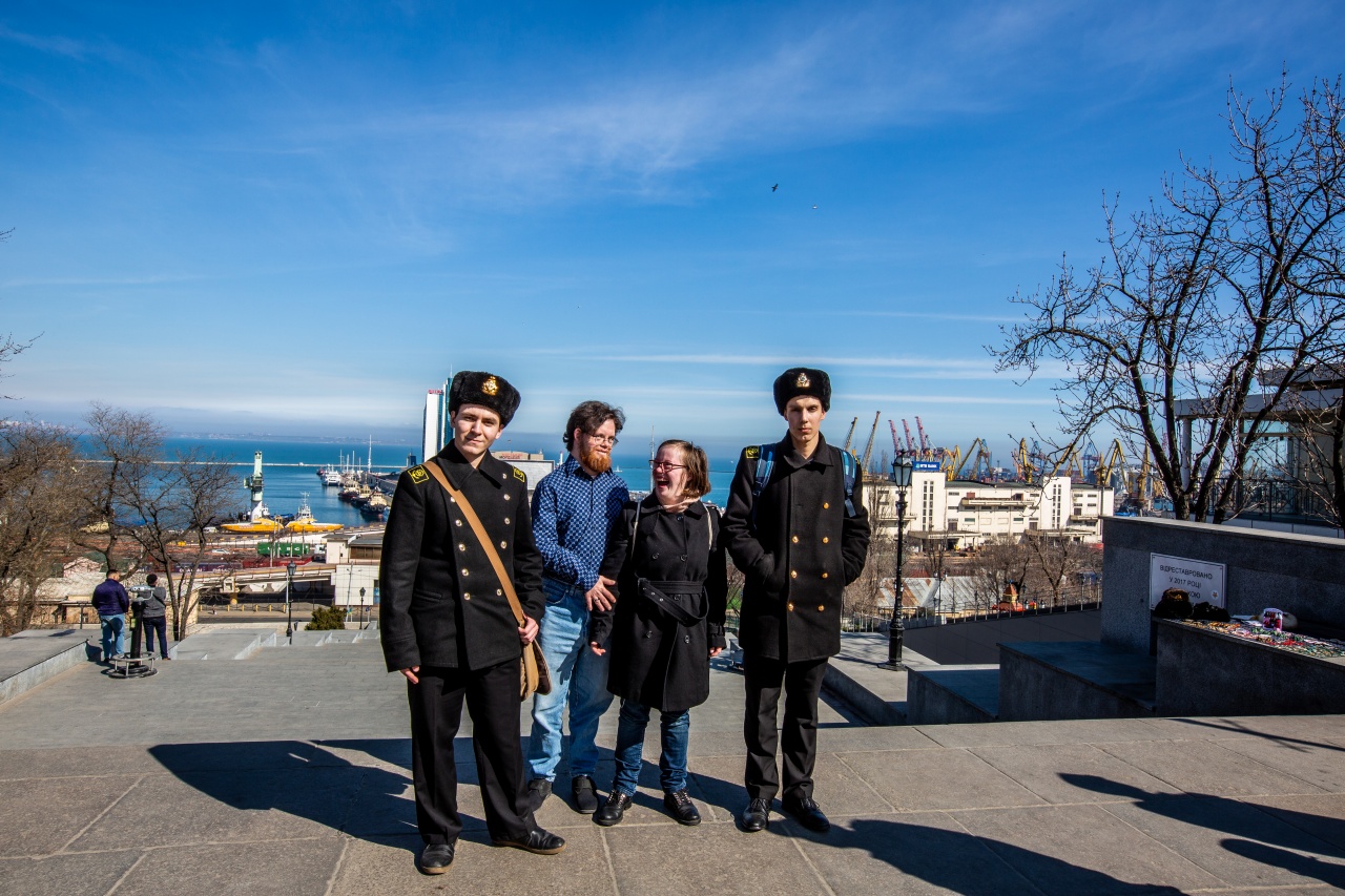 2 Männer in Marineuniform zusammen mit zwei Menschen mit Down-Syndrom. Sie stehen vor einem Abhang, darunter sieht man die Stadt Odessa.