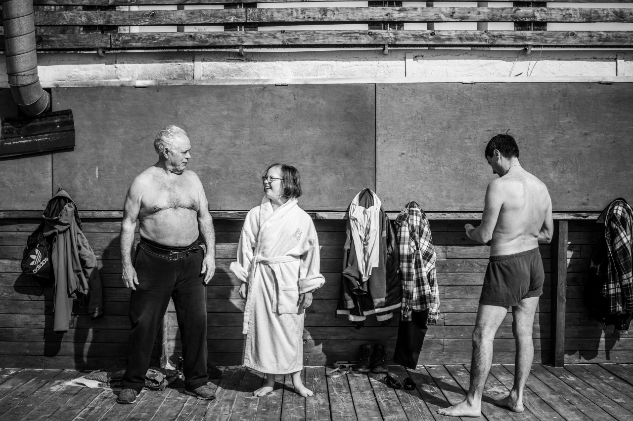 Eine Frau mit Down-Syndrom steht in einem weißen Frottee-Bademantel zwischen zwei Männern in Badehose.