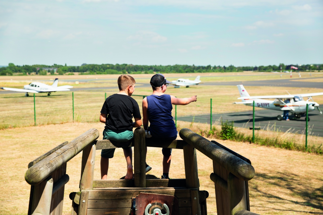 Die Brüder Matteo und Valentina Zandegiocomo sitzen mit dem Rücken zur Fotografin auf einem Holzgerüst und schauen sie Flugzeuge an