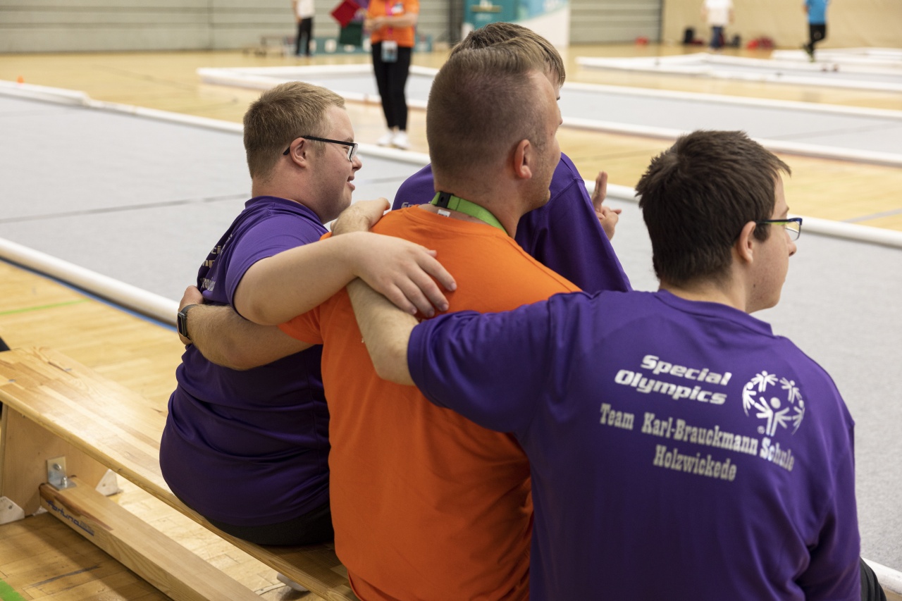 Drei Männer in Shirts mit dem Logo von Special Olympics sitzen nebeneinander auf einer Bank in einer Sporthalle.