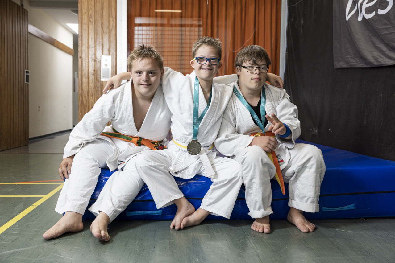 Drei Jugendliche in Judoanzügen sitzen auf einer blauen Sportmatte in einer Halle.