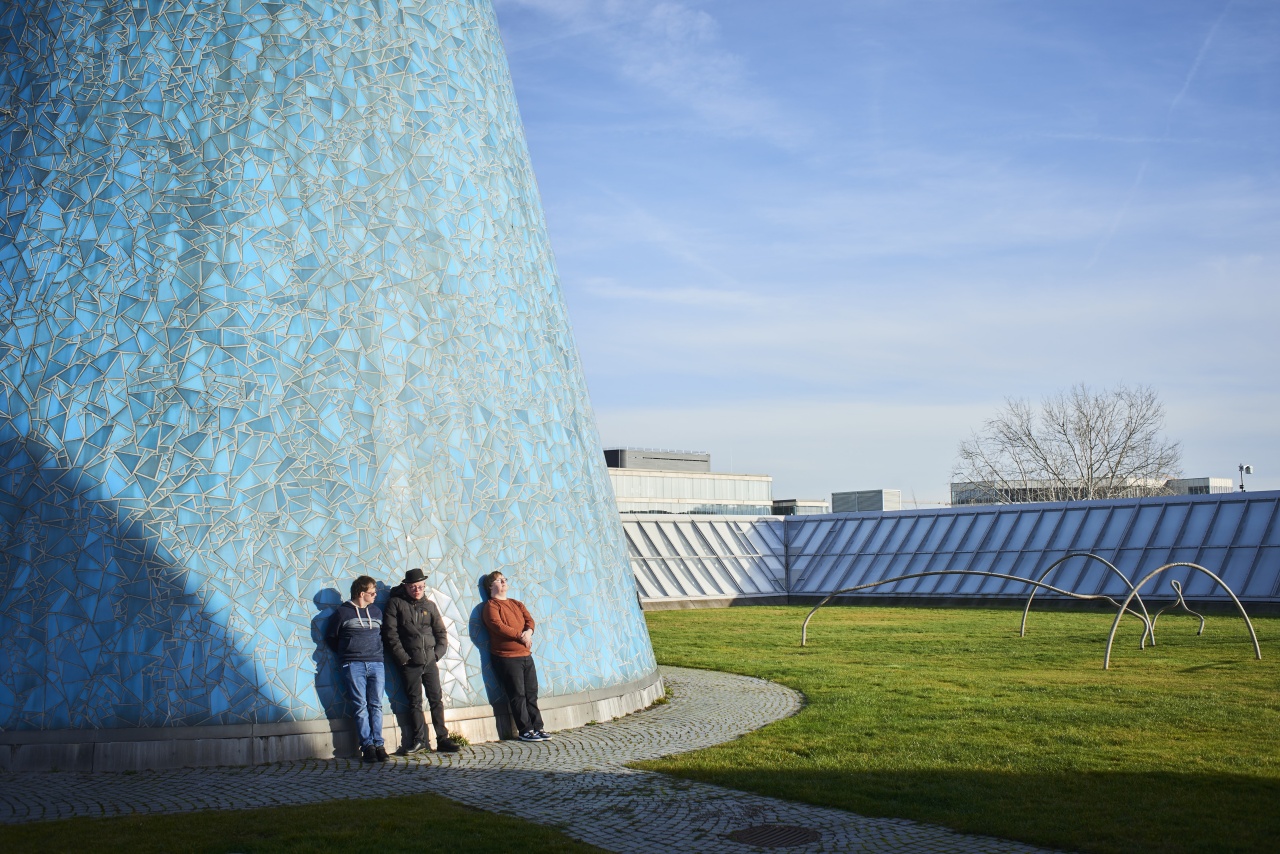 Drei Personen mit Down-Syndrom stehen auf dem Dach der Bundeskunsthalle vor einer der Spitzen mit türkisfarbenen Fliesen.
