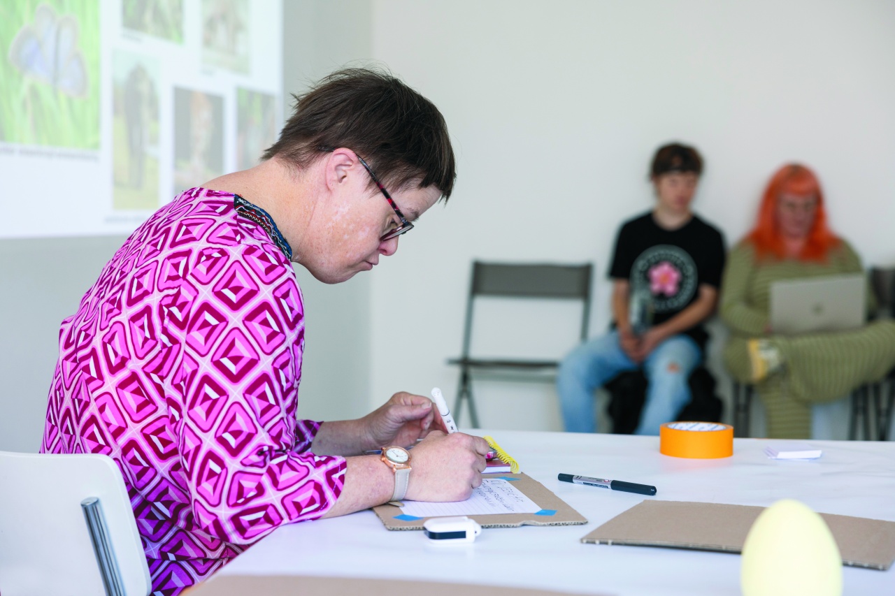 Eine Frau mit Down-Syndrom sitzt am Tisch und schreibt mit der Hand.