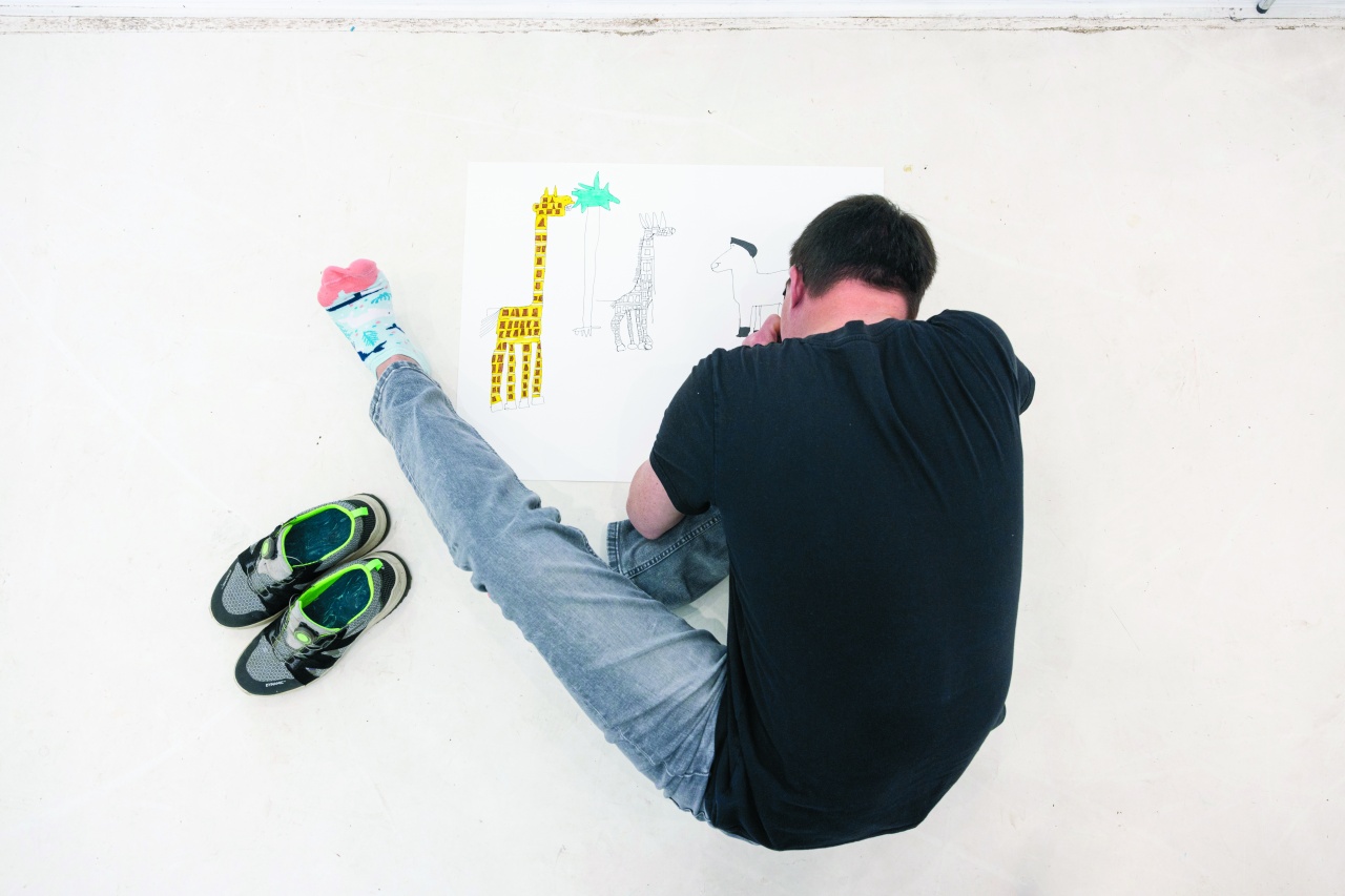 Ein Mann sitzt auf dem Boden und malt ein Bild von einer Giraffe.