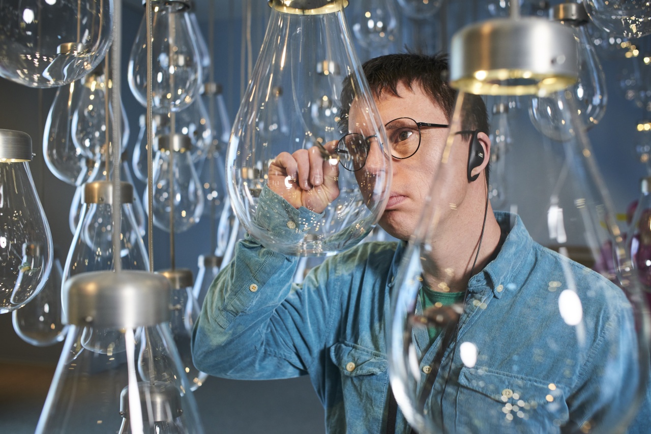 Ein Ohrenkuss-Autor steht zwischen großen Glaskolben, in denen sich künstliche Insekten befinden. Er hat seine Hand konzentriert an der Brille und betrachtet das Kunstwerk.