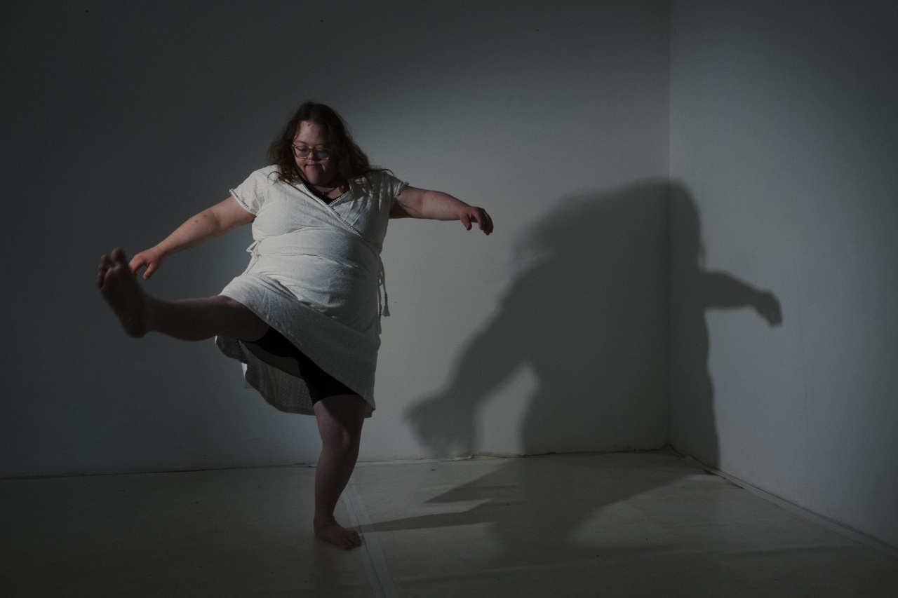 Eine Frau mit Down-Syndrom hebt das Bein und streckt die Arme von sich. Hinter ihr an der Wand sieht man ihren Schatten.