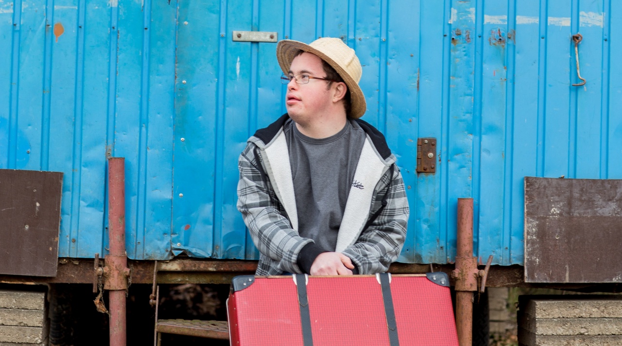 Daniel sitzt vor einem blauen Container mit Sonnenhut und Brille