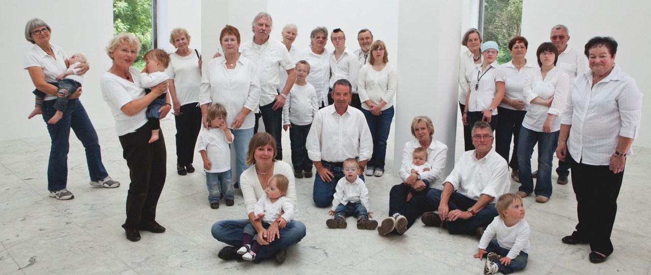 Alle Großeltern mit ihren Enkeln sind in einer Halle zu sehen, alle tragen weiße Oberteile und dunkle Hosen