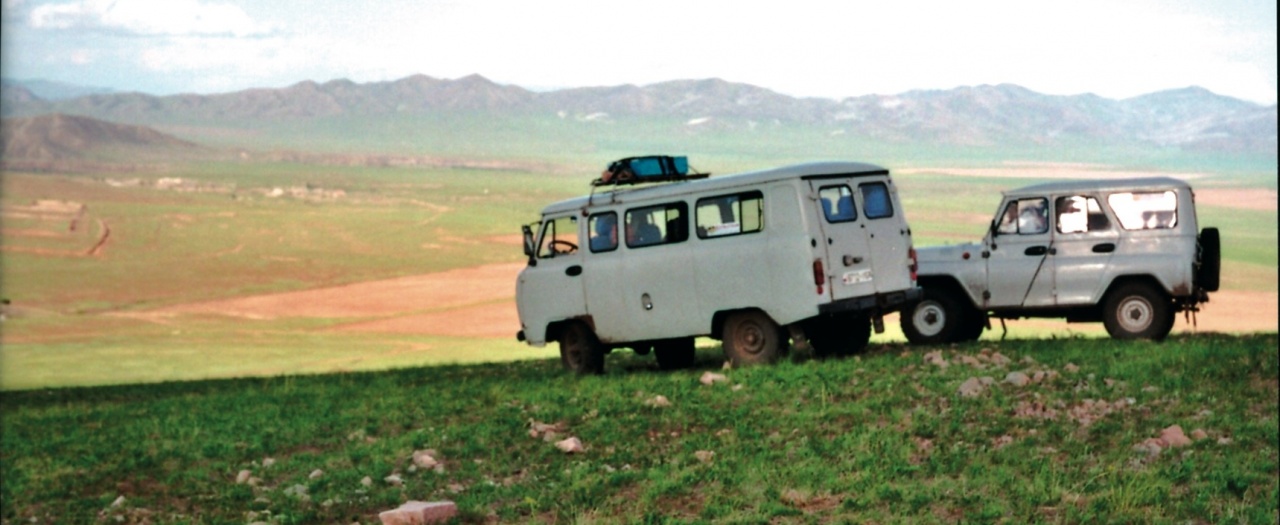 Ein weißer Bus und ein weißer Jeep stehen vor einer weitläufigen Landschaft