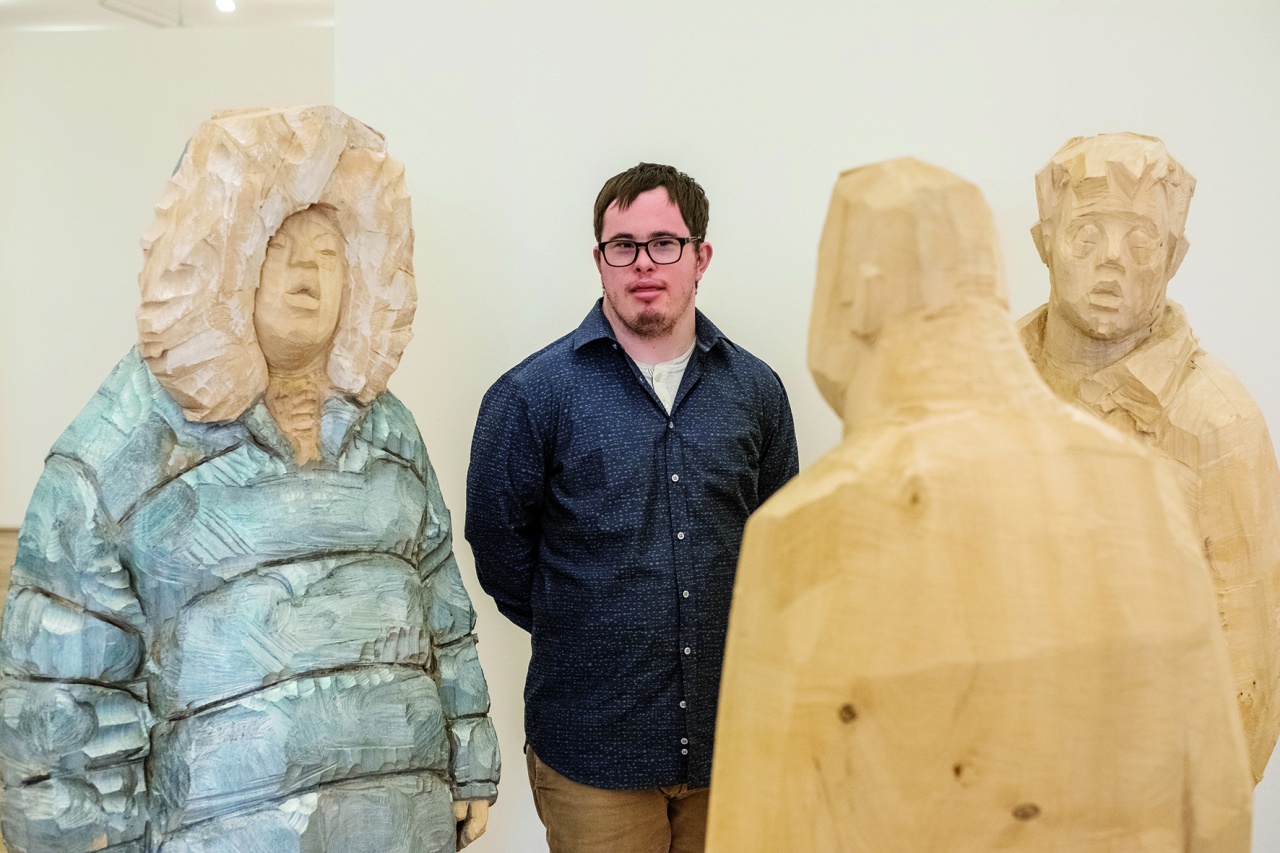 Autor Daniel Rauers steht zwischen drei Holzskulpturen des Künstlers Markus Keller