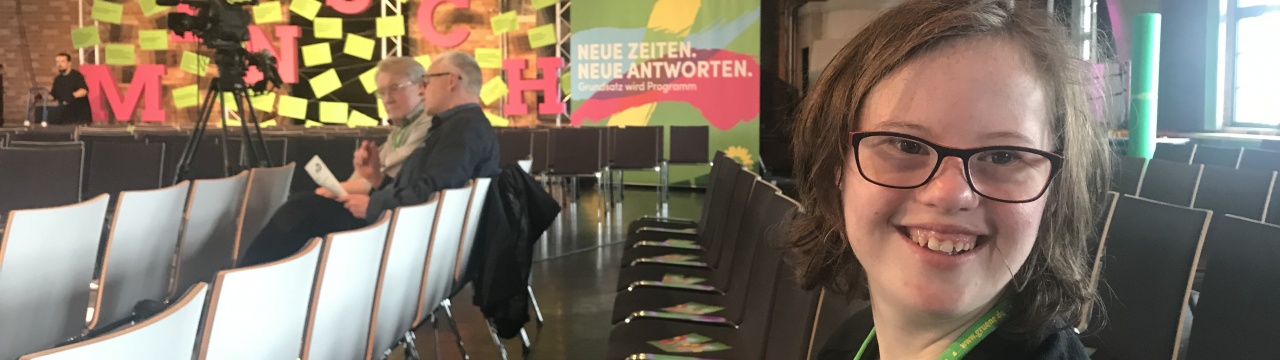 Natalie Dedreux beim Startkonvent der Partei Die Grüne: Sie sitzt in einem bestuhlten Saal, im Hintergrund ein Banner mit dem Text: Neue Zeiten. Neue Antworten.
