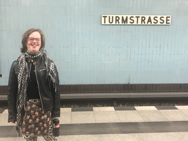Natalie Dedreux an der U-Bahn-Haltestelle Turmstraße: Hellblaue Kacheln im Hintergrund, Natalie Dedreux lächelt und hält eine Flasche Cola light in der Hand.