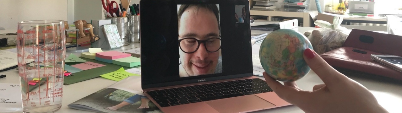 Ein aufgeklappter Laptop, der per Facetime das Livebild von Daniel Rauers zeigt. Neben dem Laptop sieht man eine Hand, die eine Weltkugel hält.