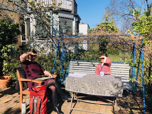 2 Frauen, eine mit und eine ohne Down-Syndrom, sitzen im Garten an einem Tisch und beschatten sich das Gesicht mit den Augen.