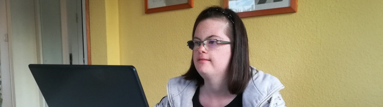 Eine junge Frau mit Down-Syndrom sitzt am Laptop.