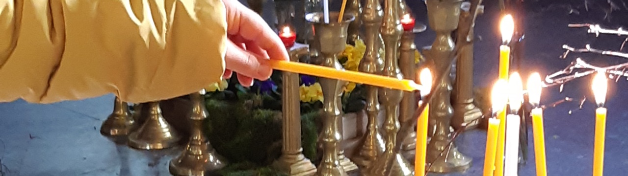 Eine Hand zündet eine Kerze an einer anderen Kerze an. Im Hintergrund brennen schon einige Kerzen.