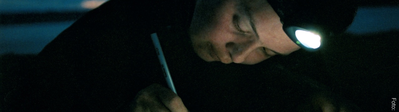 Angela Fritzen schreibt im Dunkeln, das Papier wird von einer Stirnlampe auf ihrem Kopf beleuchtet.
