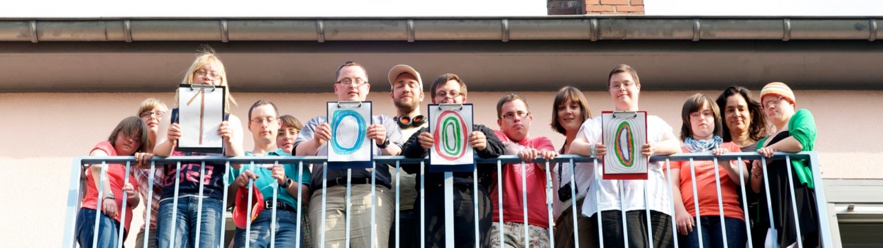 Das Ohrenkuss-Team steht auf dem Balkon und hält Schilder mit der Zahl 1.000 hoch