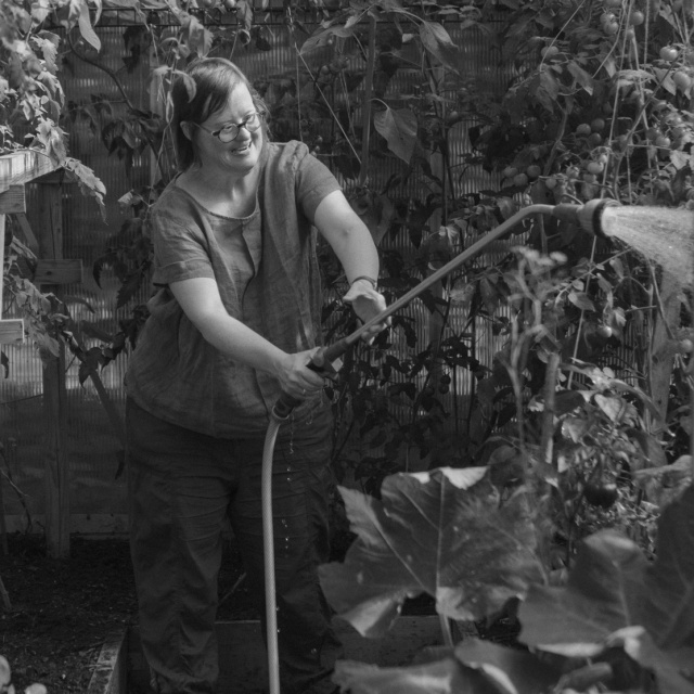 Schwarz-weiß-Foto einer Frau mit Down-Syndrom, die mit einem Schlauch Tomatenpflanzen wässert.